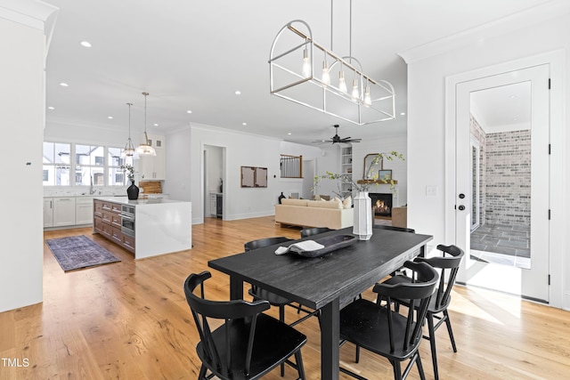 dining space featuring ornamental molding, a lit fireplace, light wood finished floors, and ceiling fan with notable chandelier