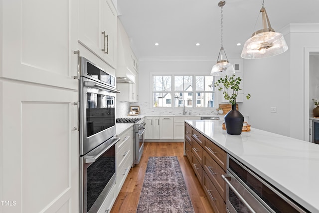 kitchen with light countertops, appliances with stainless steel finishes, light wood-style floors, ornamental molding, and white cabinets