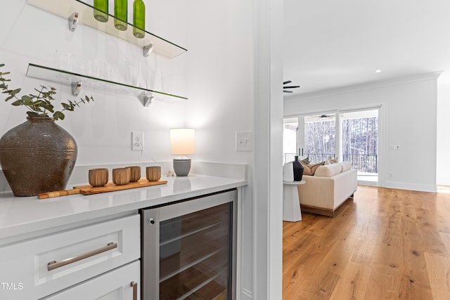 bar featuring a dry bar, beverage cooler, baseboards, ornamental molding, and light wood-style floors