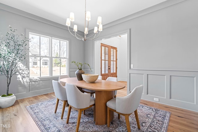 dining space with light wood-type flooring, french doors, a decorative wall, and an inviting chandelier