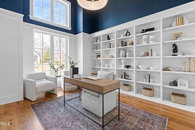 home office with a towering ceiling, built in shelves, wood finished floors, and a wealth of natural light