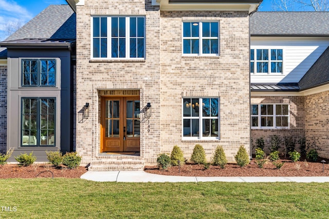 property entrance featuring a yard, french doors, brick siding, and a standing seam roof