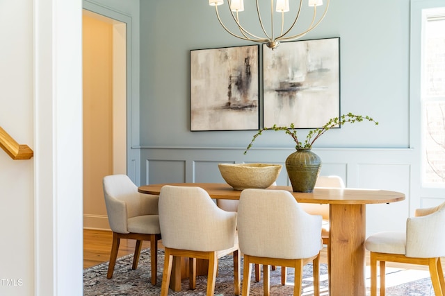 dining room featuring a wainscoted wall, an inviting chandelier, wood finished floors, and a decorative wall