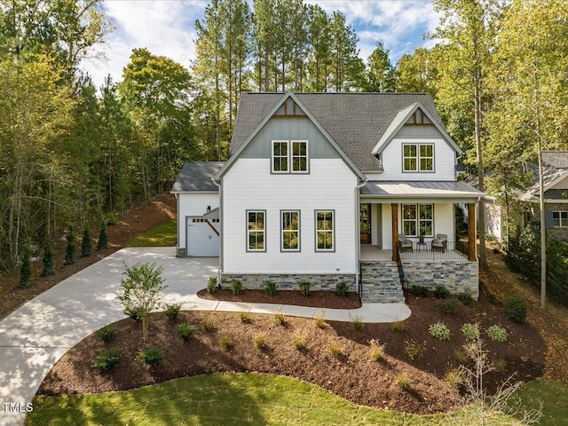 view of front of home with metal roof, covered porch, a shingled roof, concrete driveway, and a standing seam roof