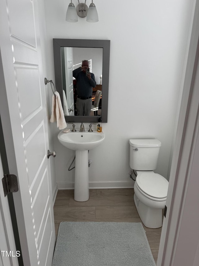 half bathroom with toilet, a sink, baseboards, and wood finished floors