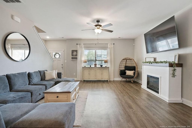 living area featuring visible vents, baseboards, a ceiling fan, a glass covered fireplace, and wood finished floors