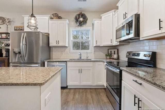 kitchen featuring stainless steel appliances, backsplash, white cabinetry, a sink, and light wood-type flooring