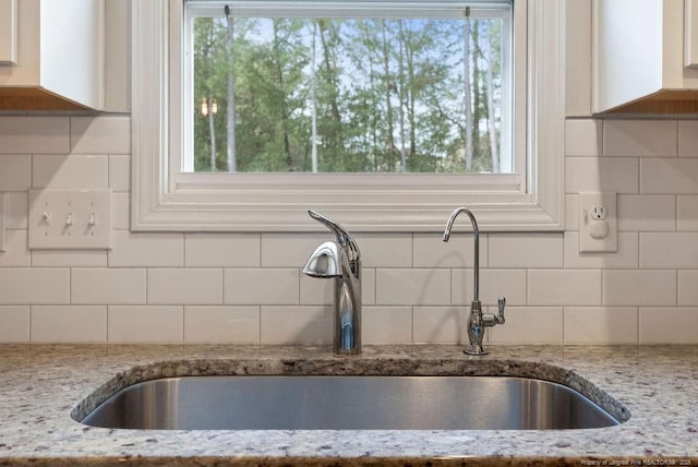 kitchen with tasteful backsplash, a sink, a wealth of natural light, and light stone countertops