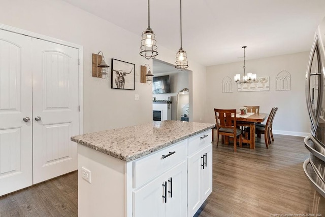 kitchen with a kitchen island, hanging light fixtures, freestanding refrigerator, light stone countertops, and dark wood-style floors