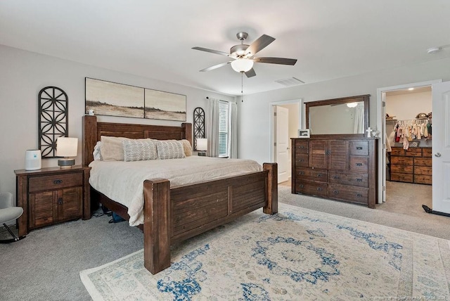 bedroom with carpet floors, a walk in closet, visible vents, and a ceiling fan