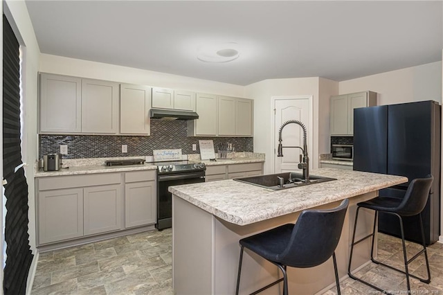 kitchen with under cabinet range hood, gray cabinetry, range with electric stovetop, a sink, and a kitchen breakfast bar