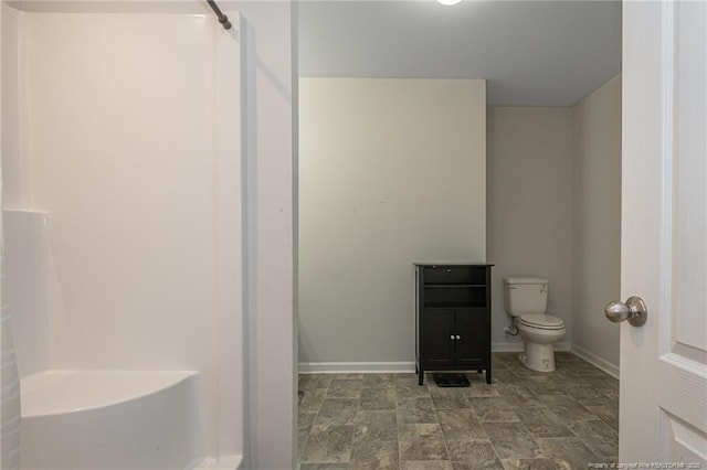 bathroom with toilet, stone finish flooring, baseboards, and a shower