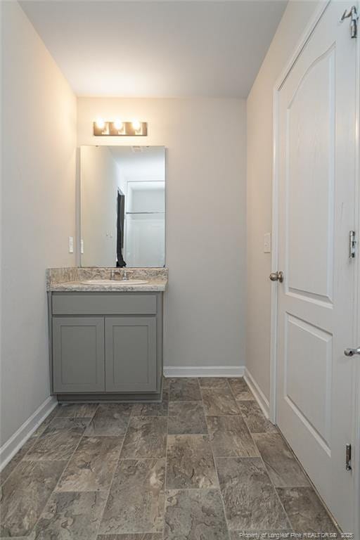 bathroom featuring stone finish flooring, vanity, and baseboards