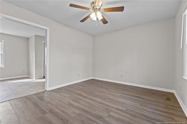 unfurnished room featuring visible vents, wood finished floors, a ceiling fan, and baseboards