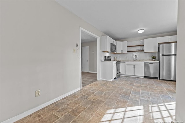 kitchen with a sink, light countertops, appliances with stainless steel finishes, open shelves, and tasteful backsplash