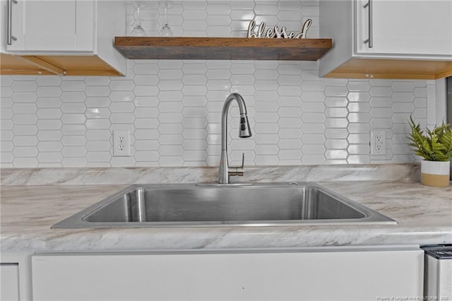 room details featuring open shelves, decorative backsplash, white cabinetry, a sink, and light stone countertops