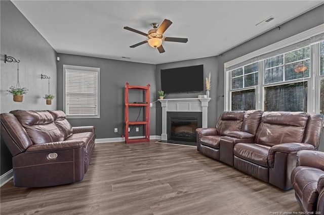 living area with baseboards, visible vents, a ceiling fan, a fireplace with flush hearth, and wood finished floors