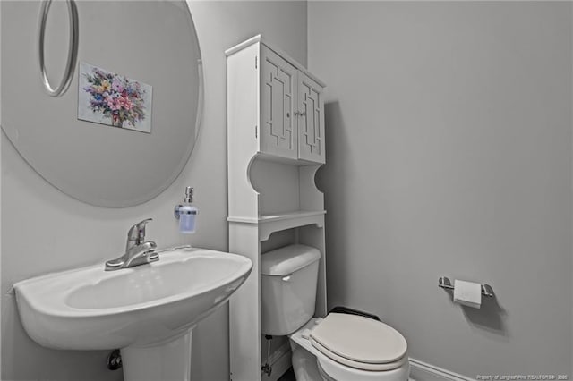 half bath with baseboards, a sink, and toilet