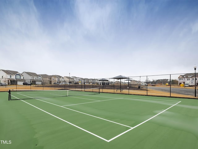 view of tennis court featuring community basketball court, fence, and a residential view