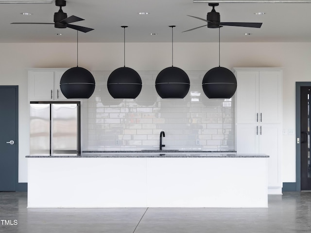 kitchen with decorative light fixtures, a ceiling fan, a kitchen island with sink, white cabinets, and dark stone countertops