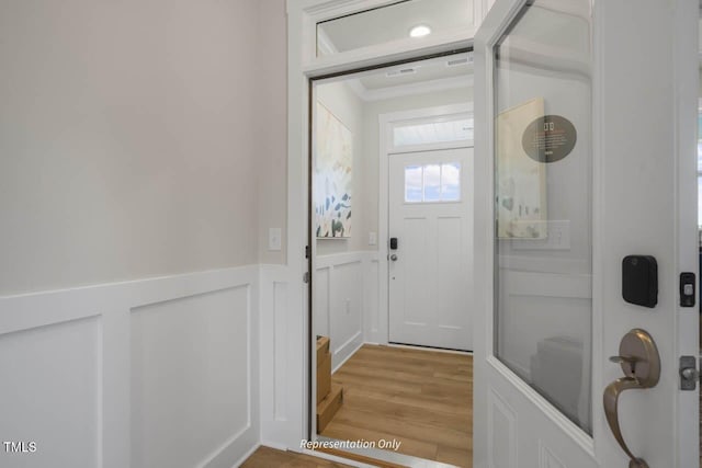 interior space with ornamental molding, wainscoting, a decorative wall, and light wood finished floors