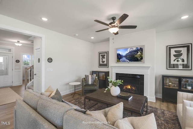 living area featuring recessed lighting, stairway, wood finished floors, a lit fireplace, and baseboards