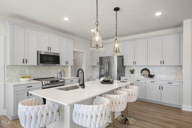 kitchen with a kitchen island with sink, a breakfast bar, a sink, light countertops, and appliances with stainless steel finishes