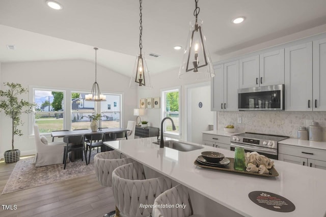 kitchen with decorative backsplash, lofted ceiling, appliances with stainless steel finishes, wood finished floors, and a sink