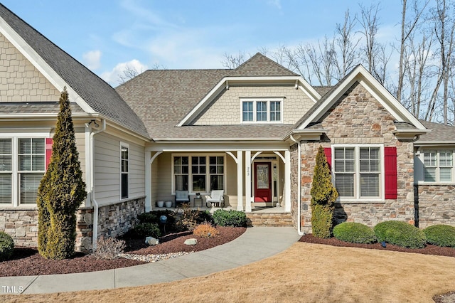 craftsman-style house with covered porch, stone siding, and a shingled roof