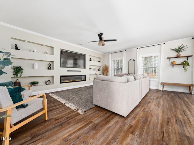 living room featuring ornamental molding, built in features, wood finished floors, a glass covered fireplace, and baseboards