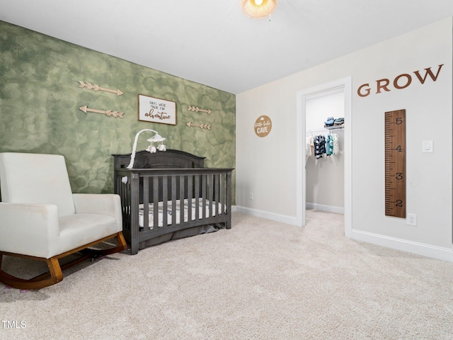 carpeted bedroom with a crib, a walk in closet, and baseboards