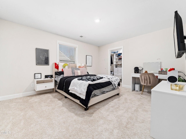 bedroom featuring light colored carpet, a walk in closet, and baseboards