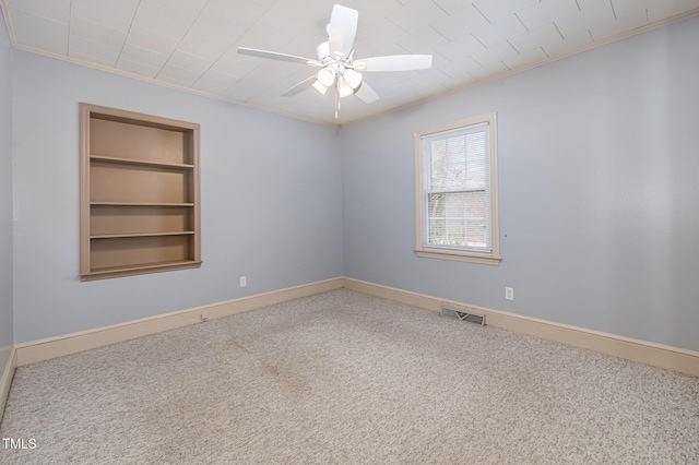 carpeted spare room with visible vents, crown molding, ceiling fan, baseboards, and built in features