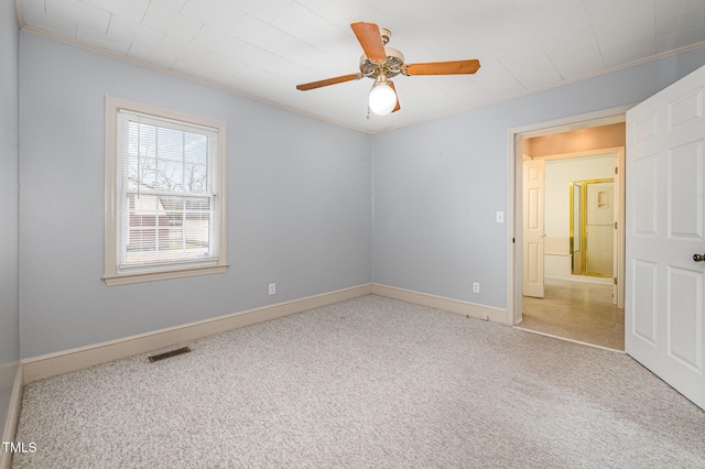 carpeted spare room with visible vents, ceiling fan, crown molding, and baseboards