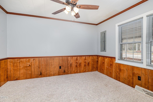 carpeted spare room featuring a wainscoted wall, visible vents, wood walls, and ornamental molding