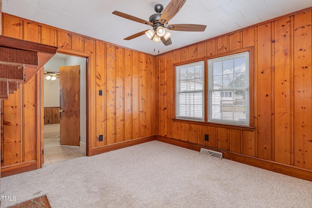 carpeted empty room with a ceiling fan, visible vents, and wood walls