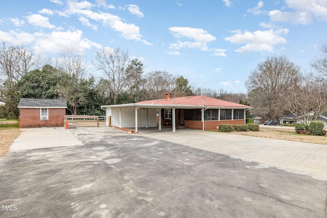 view of front of house with concrete driveway, an outdoor structure, brick siding, and a sunroom