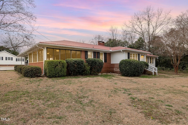 ranch-style house with brick siding, a lawn, a chimney, and a sunroom