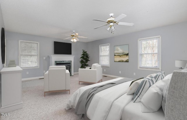 bedroom featuring ceiling fan, a premium fireplace, baseboards, and light carpet