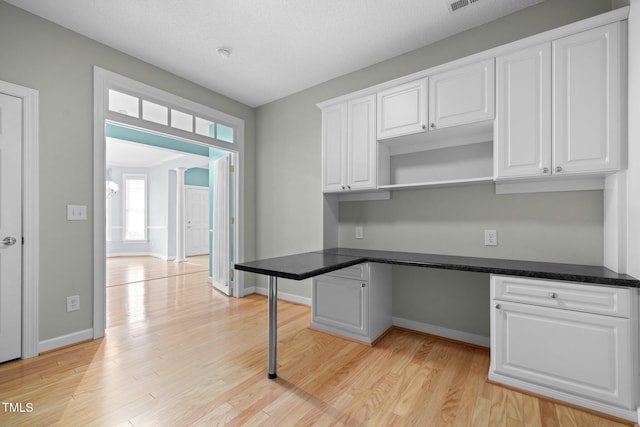 kitchen featuring light wood finished floors, built in desk, and white cabinets