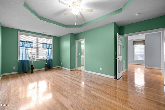 unfurnished room with baseboards, a tray ceiling, wood finished floors, a textured ceiling, and a ceiling fan