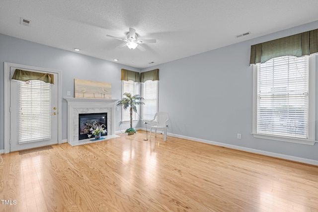 unfurnished living room featuring plenty of natural light, light wood-style flooring, baseboards, and a premium fireplace