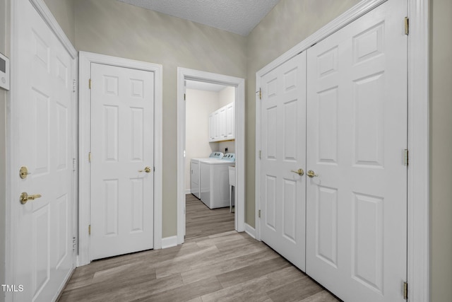 hall featuring separate washer and dryer, baseboards, light wood finished floors, and a textured ceiling