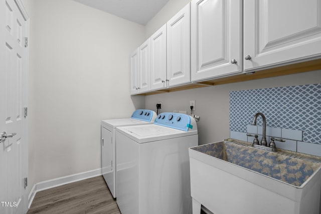 laundry area with a sink, wood finished floors, washing machine and dryer, cabinet space, and baseboards