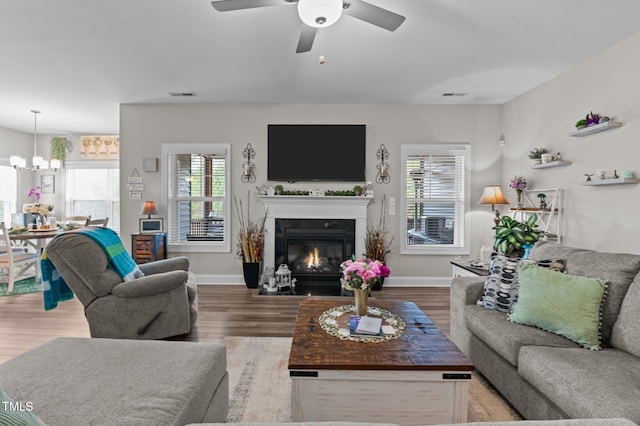 living area featuring a fireplace with flush hearth, wood finished floors, visible vents, and baseboards