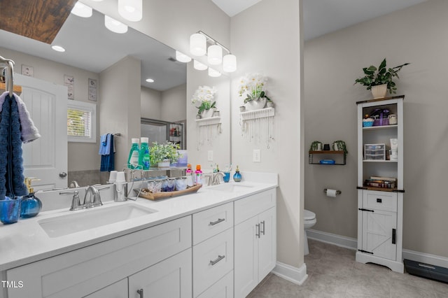 bathroom featuring toilet, double vanity, baseboards, and a sink