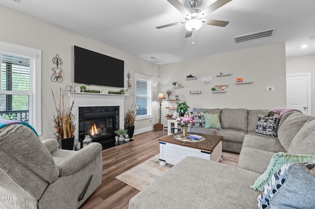 living area with a fireplace with flush hearth, a wealth of natural light, visible vents, and wood finished floors