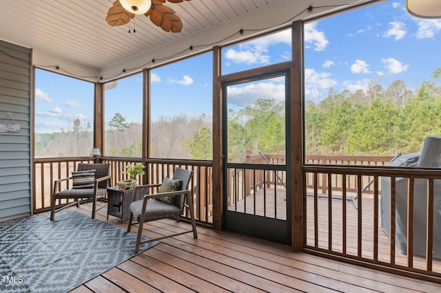 sunroom with a forest view and a ceiling fan