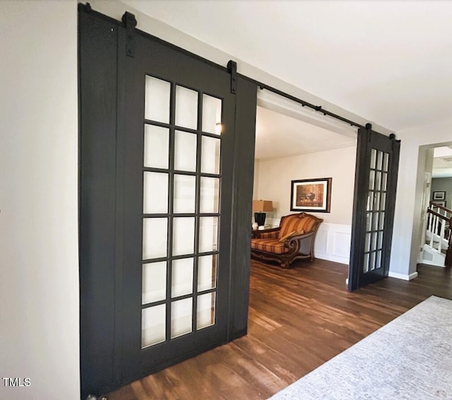 interior space with a wainscoted wall, a barn door, a decorative wall, and wood finished floors