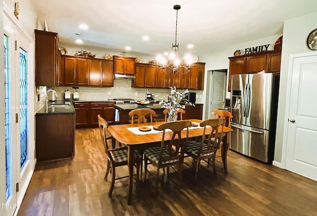 kitchen featuring a sink, stainless steel refrigerator with ice dispenser, tasteful backsplash, dark countertops, and dark wood finished floors